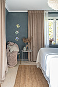 A side table in front of a beige curtain in a bedroom with a grey wall