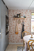 A fitted kitchen with grey fronts, a round dining table and pink patterned wallpaper on the wall
