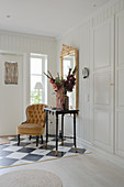 An upholstered chair, an antique table and a gold-framed mirror in a hallway