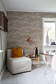 A covered armchair and a side table in front of patterned wallpaper in the corner of a room