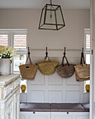 A selection of French wicker shopping baskets on iron coat hooks in boot room with pendant lamp