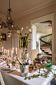 Christmas table festively set with lilies and mercury glass candlesticks below antique copper chandelier