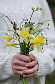 Woman holding bouquet of narcissus, snowdrops and cornelian cherry