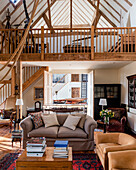Double height living room with antique telescopes on mezzanine and suede armchairs in barn conversion