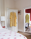 Calm guest bedroom in fuchsia and white , a brightly coloured pasha hangs from the back of the door and there is an open doorway to the ensuite bathroom