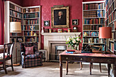 Antique, Victorian desk and bookshelves in study with red ornate wallpaper