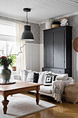 Black wardrobe, light-coloured upholstered sofa and wooden coffee table in the living room