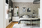 Old metal twin beds below black-and-white photographs on wallpapered wall