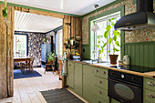 Kitchen unit with green cupboards and rustic wooden wall between kitchen and dining room