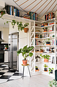 Shelves of houseplants and books next to and above doorway leading into kitchen