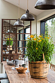 Dining room with large wicker basket with yellow flowers on wooden table and industrial hanging lamps