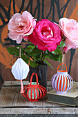 Handmade coloured paper lanterns hung from vase of roses