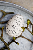 Egg covered in lettered fabric surrounded by budding twigs
