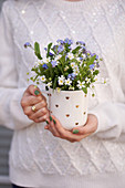 Woman holding a mug with a spring bouquet of chickweed and forget-me-nots