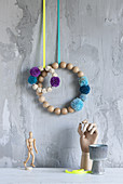 Wreaths of wooden beads and pompoms hung on wall with grey, structured, plaster surface