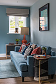 Blaues Sofa mit Kissen in Rostrot vor hellblauer Wand im Wohnzimmer