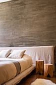 Holzhocker neben dem Bett vor einer Wand mit Beton Brut
