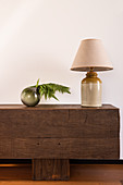 Table lamp and fern leaves in spherical vase on bench made of wooden beams