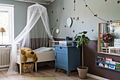 Nursery painted in green and brown, bed with canopy and chest of drawers