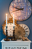 Antique wall clock above dials and candles on top of white cabinet