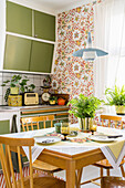Dining area in front of floral wallpaper in retro kitchen with green fronts