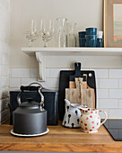 Kettle, jugs and cutting boards under kitchen shelf