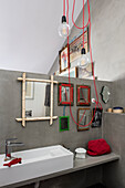 Light fixture with red cables in bathroom with collection of mirrors on grey wall