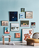 Framed pictures on light blue wall, stool and armchair in front of it