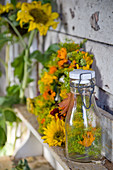 Flasche mit Fenscheldolden und Ringelblumenblüten, dahinter Herbstkranz