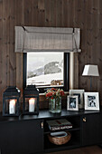 Lanterns, bouquet of flowers and photos on black low sideboard below window