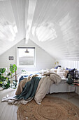 Doppelbett und Grünpflanze im Schlafzimmer mit weiß lackierter Holzverkleidung