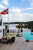 Haus mit Terrasse, Pool und norwegischer Fahne am Wasser