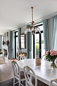White dining table and chairs in open-plan interior with French windows and blue curtains