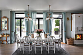 White dining table with chairs in open living room with French doors and blue curtains