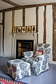 Loose-covered armchair with matching footstool in front of fireplace in bedroom with wooden beams