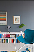 Blue armchair in front of bookshelves in lounge with dark wall