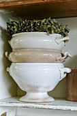 Stack of old soup tureens and wreath of dried flowers on shelf