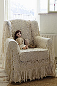 Doll on armchair with crocheted throw