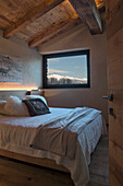 Double bed and picture window in bedroom with wood-beamed ceiling