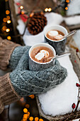 Gloved hands holding hot chocolate with marshmallows