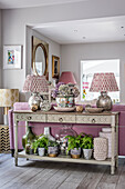 Konsolentisch mit Tischlampen, Hortensie und Topfpflanzen an rosa Couch