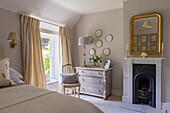 Gilt-framed mirror over fireplace and antique, decorative wall plates over restored chest of drawers in bedroom