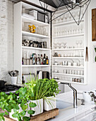Glasses, crockery and kitchen utensils on white shelves in kitchen