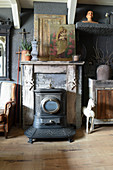 Old stove in front of fireplace with religious painting on mantelpiece and vintage-style accessories
