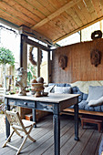 Alter Tisch und Bank auf überdachter Terrasse mit Vintage-Deko