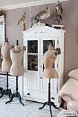 Old tailors' dummies in front of white glass-fronted cabinet with stuffed birds on top