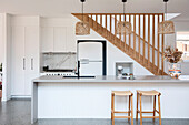 Long kitchen counter with bar stools in front of staircase wall and wooden staircase