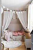 Bed with curtains and round rug in girl's bedroom in muted colours