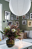 Bouquet of flowers on coffee table and gallery of photos on green wall in background