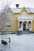 Yellow wooden house with balcony and veranda in snowy garden